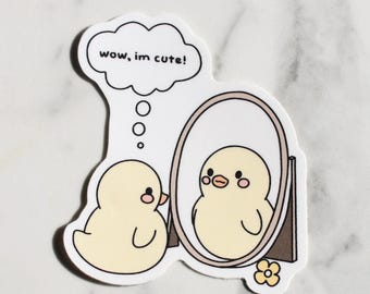 Può includere: Un adesivo fustellato con un pulcino dei cartoni animati che si guarda allo specchio. Il pulcino è giallo con guance rosa e un piccolo becco arancione. Una nuvoletta sopra il pulcino dice: "wow, im cute!". Un piccolo fiore in basso.