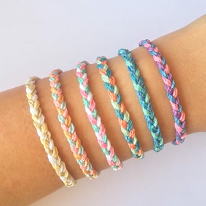 Può includere: Sette braccialetti dell'amicizia intrecciati colorati in varie tonalità di blu, verde, rosa e giallo.