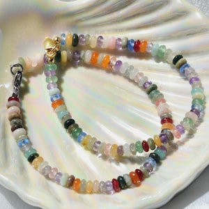 May include: A multi-colored beaded necklace with a variety of stones, including green, blue, red, orange, and pink. The necklace is made of small, round beads and is strung on a silver chain.