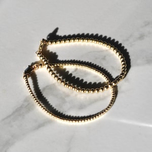 May include: Two gold beaded bracelets, one slightly larger than the other, are stacked on top of each other. The bracelets are made of small, round beads and have a simple, elegant design.