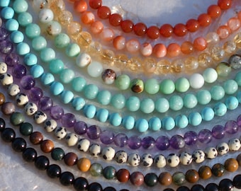 May include: Multiple strands of round gemstone beads arranged in a curved pattern. The collection includes various colors such as orange, yellow, light green, turquoise, purple, black, and white with black spots, showcasing a smooth polished finish.