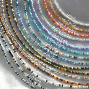 May include: A collection of 16 different beaded necklaces, each with a unique colour and pattern. The necklaces are labelled with names like "quartz", "sand dollar", "peach parfait", and "spring flowers".