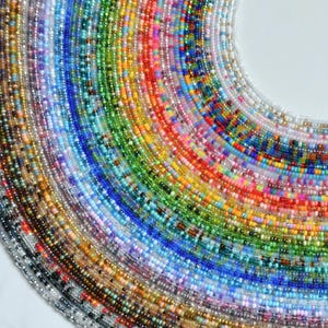 May include: A collection of multiple strands of small, round glass seed beads arranged in a semi-circular fan pattern. The beads feature a full spectrum of colors including red, orange, yellow, green, blue, indigo, violet, white, and black.