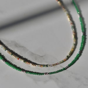 May include: Two layered necklaces with green and multi-colored beads. The top layer has smaller, multi-colored beads and the bottom layer has larger, green beads.