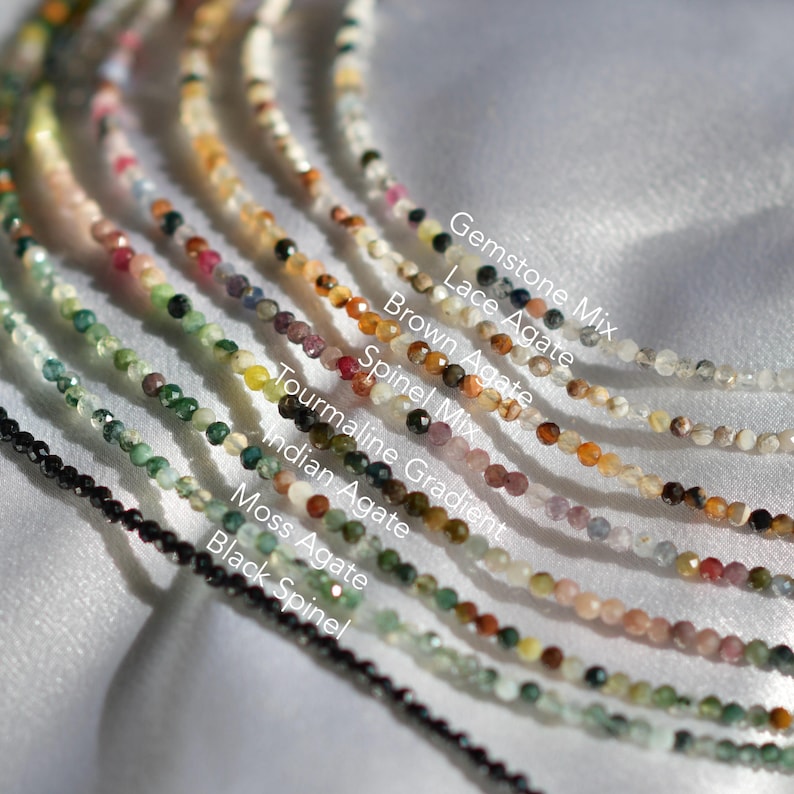 May include: A close-up of ten strands of gemstone beads, each with a different color and pattern. The beads are labeled with their names, including Gemstone Mix, Lace Agate, Brown Agate, Spinel Mix, Tourmaline Gradient, Indian Agate, Moss Agate, and Black Spinel.