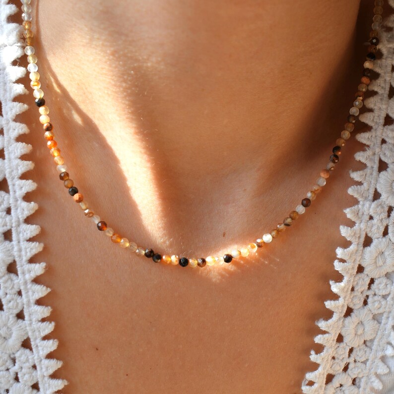 May include: A delicate necklace made of small, round, multi-colored agate beads. The beads are a mix of brown, beige, and black.