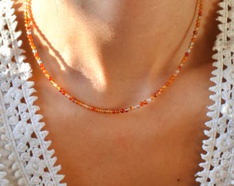 May include: A delicate necklace made of small, round carnelian beads in shades of orange and red. The beads are strung on a thin silver chain.