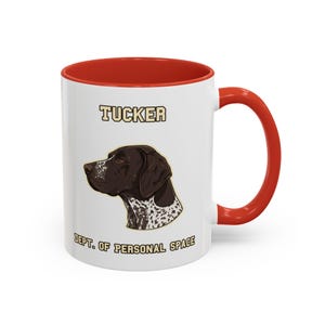 Puede incluir: Taza de cerámica blanca con interior y asa rojos. La taza presenta un gráfico de la cabeza de un perro con el nombre "Tucker" arriba y "Dept. of Personal Space" abajo. El perro es marrón y blanco.