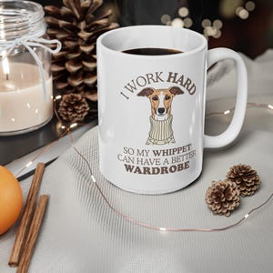 Puede incluir: Taza de cerámica blanca con el texto "I WORK HARD SO MY WHIPPET CAN HAVE A BETTER WARDROBE". La taza presenta un galgo de dibujos animados con un suéter. La taza está llena de un líquido oscuro.