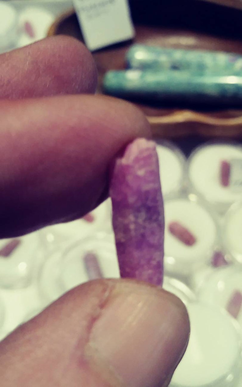 May include: A close-up of a pink and white crystal, held in a hand. The crystal is long and thin, with a smooth, polished surface.