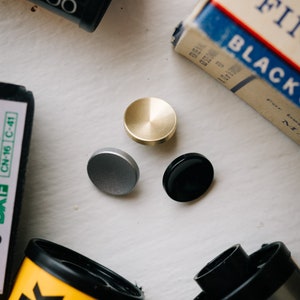 May include: Four rolls of film, two yellow, one black, and one white, with three camera lens caps: one gold, one silver, and one black. The film rolls are labeled "Kodak" and "RA 400".