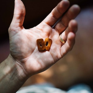 Puede incluir: Dos pequeños llaveros ovalados de cuero marrón con un agujero en el centro.