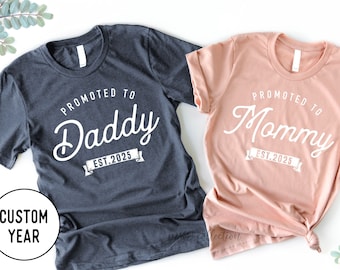 May include: Two t-shirts, one gray and one peach, with the text "Promoted to Daddy Est. 2025" and "Promoted to Mommy Est. 2025" printed on them.