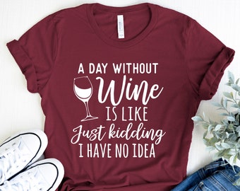 Peut inclure: Un t-shirt bordeaux avec un texte blanc qui dit "A day without wine is like just kidding I have no idea". Le t-shirt présente un graphique de verre à vin blanc.