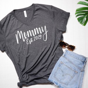 May include: A dark gray V-neck t-shirt with the text "Mommy Est. 2019" in white lettering.