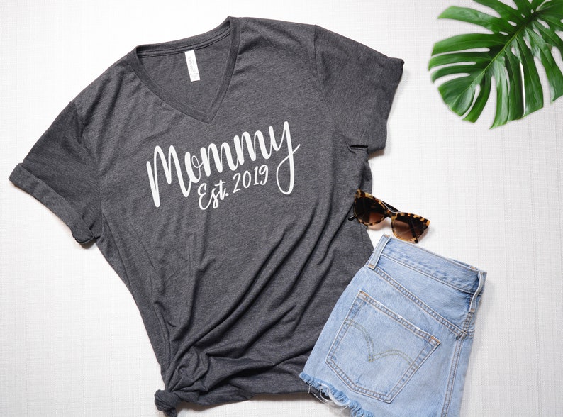 May include: A dark gray V-neck t-shirt with the text "Mommy Est. 2019" in white lettering.