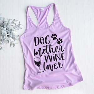 May include: A light purple racerback tank top with the words "Dog Mother Wine Lover" in black script. The design includes paw prints and a wine glass. The top is made of a soft material.