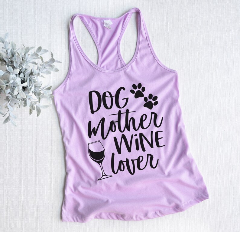 May include: A light purple racerback tank top with the words "Dog Mother Wine Lover" in black script. The design includes paw prints and a wine glass. The top is made of a soft material.