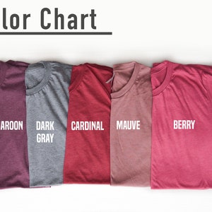 May include: A color chart displaying five folded t-shirts in various colors: H Maroon, Dark Gray, Cardinal, Mauve, and Berry. The text "Color Chart" is at the top. The shirts are arranged on a white surface.