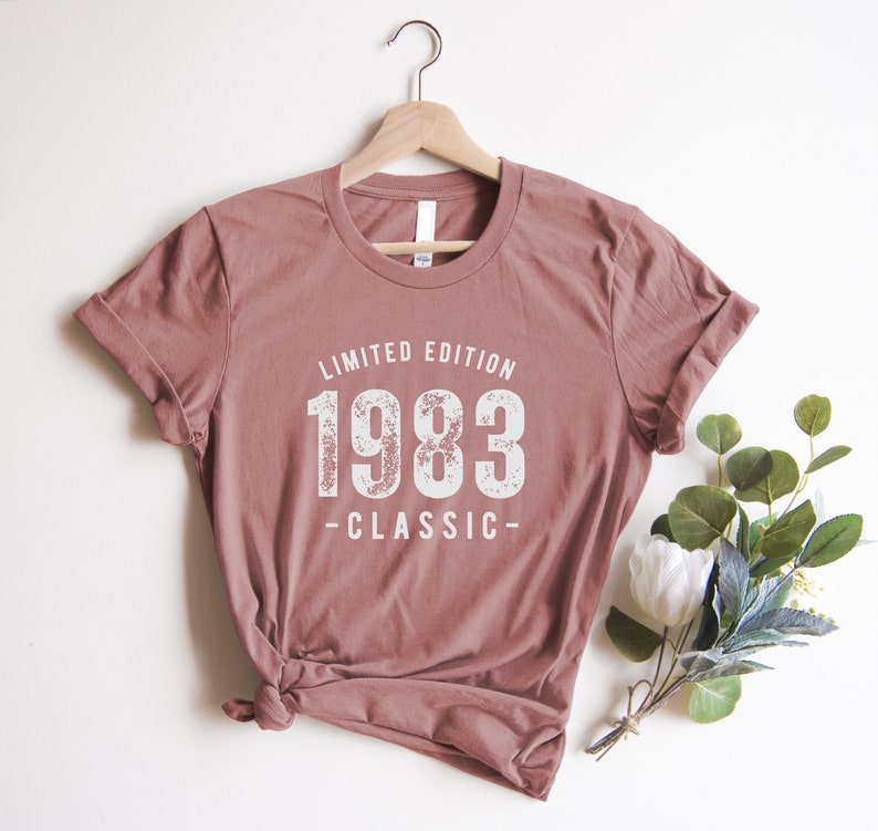 May include: A mauve colored t-shirt with a white graphic that says "Limited Edition 1983 -Classic-"