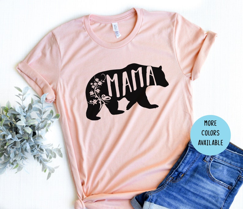 Puede incluir: Camiseta rosa con una silueta de oso negro y la palabra "MAMA" dentro del oso. El oso tiene detalles florales a su alrededor.