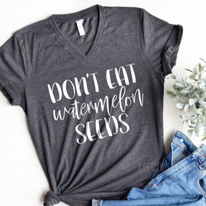Puede incluir: Una camiseta gris oscuro de cuello en V con el texto "Don't eat watermelon seeds" impreso en blanco.