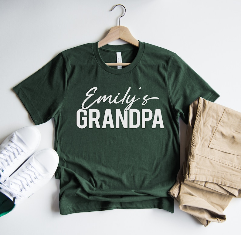 以下が含まれることがあります： 白い文字で「Emily's GRANDPA」と書かれた濃い緑色のTシャツです。