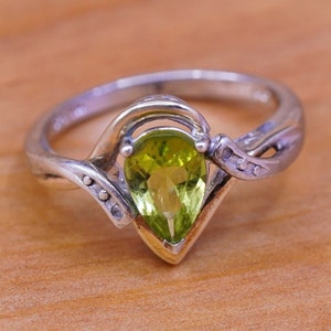 May include: A silver ring with a pear-shaped, light green gemstone. The ring has a unique design with a gold-colored base and decorative silver accents. The gemstone is the focal point, showcasing its vibrant color and cut.