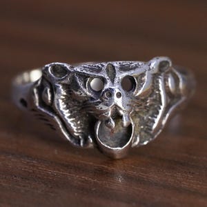 May include: A silver-toned metal ring featuring a sculpted animal head design with prominent ears, hollowed-out eyes, and a small circular opening below the mouth. The surface has a polished finish with darkened recessed areas to highlight the details.
