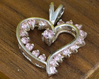 Peut inclure: Pendentif en forme de cœur argenté orné de pierres roses. Le pendentif a une forme de cœur avec une bélière pour une chaîne. De petites pierres roses sont serties autour du contour du cœur, avec une pierre plus grande au centre.