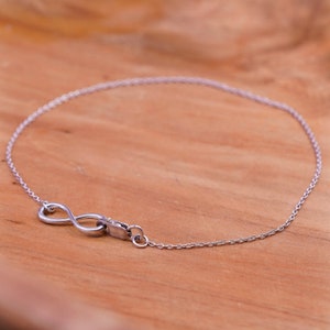 May include: A delicate silver bracelet featuring an infinity symbol charm. The bracelet is made of a fine chain and has a secure clasp. The infinity symbol is a prominent design element.