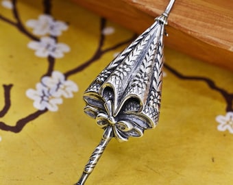 Peut inclure: Un pendentif en forme de parapluie argenté détaillé. Le parapluie présente des motifs floraux et géométriques complexes, avec un détail de nœud à la base. La poignée est torsadée et le pendentif a une petite pointe arrondie. Le fond est une surface jaune avec un motif floral.