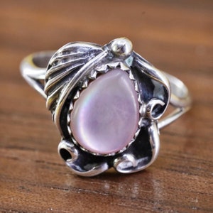 May include: Sterling silver ring featuring a pear-shaped, iridescent, light pink gemstone. The gemstone is set within a decorative, leaf-like setting. The ring has a split shank design and a polished finish.