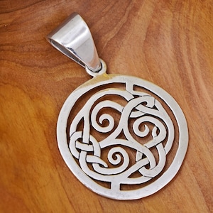 May include: A silver pendant with a Celtic knot design. The pendant is circular with an intricate, openwork pattern of interwoven lines and swirls. It has a polished finish and a bail for attaching to a chain. The pendant is displayed on a wooden surface.