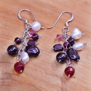 May include: A pair of dangle earrings with a cluster of beads. The earrings feature a silver hook and are adorned with a mix of dark purple, red, pink, and white beads. The beads include round, oval, and rectangular shapes.