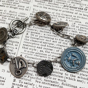 May include: A silver charm bracelet with various charms, including a key, a bird, and a flower. The bracelet is on a book with text about romance.