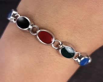 Puede incluir: Una pulsera de plata con cuatro piedras ovaladas. Las piedras son negras, rojas, verdes y azules.