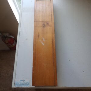 Puede incluir: Una caja de madera con una pequeña ventana en la parte superior. La caja está hecha de madera marrón claro y tiene un acabado natural. La caja está sobre una superficie blanca. El texto en la caja dice: "Cuando la temperatura ambiente y la humedad relativa son altas, puede haber escarcha o rocío de agua en el borde de la puerta y la abertura del congelador, límpielo con un paño seco."