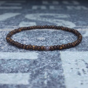Puede incluir: Un brazalete de cuentas marrones con una sola cuenta gris en el centro.