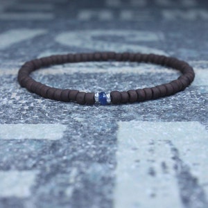 Puede incluir: Un brazalete de cuentas marrones con un solo acento de piedra preciosa azul.
