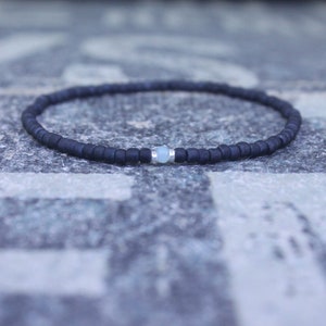 Könnte beinhalten: Ein schwarzes Perlenarmband mit einem einzigen hellblauen Edelsteinakzent.