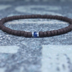 Puede incluir: Un brazalete de cuentas marrones con un solo acento de piedra preciosa azul.
