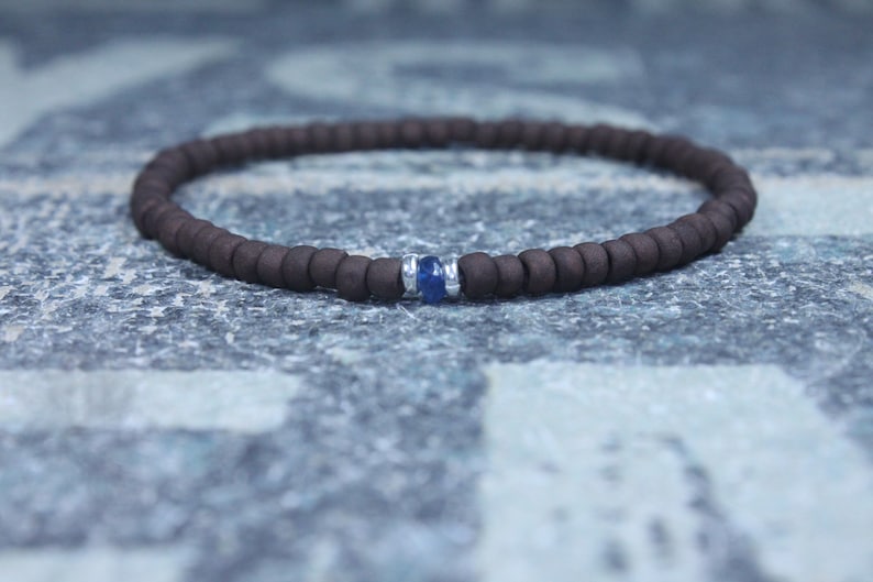 Puede incluir: Un brazalete de cuentas marrones con un solo acento de piedra preciosa azul.