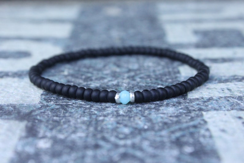 May include: A black beaded bracelet with a single light blue gemstone bead.