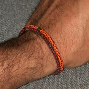 May include: Two bracelets on a person's wrist. The bracelets are made of small beads in shades of orange, red, and brown.