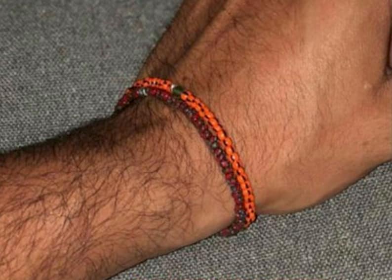 May include: Two bracelets on a person's wrist. The bracelets are made of small beads in shades of orange, red, and brown.