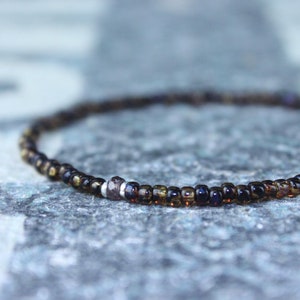 May include: A delicate bracelet made of small, dark brown glass beads with a single silver bead accent.