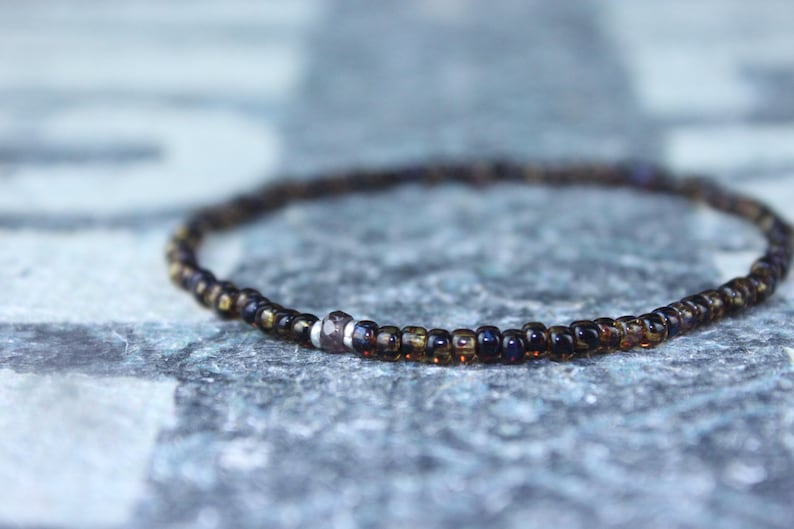May include: A delicate bracelet made of small, dark brown glass beads with a single silver bead accent.