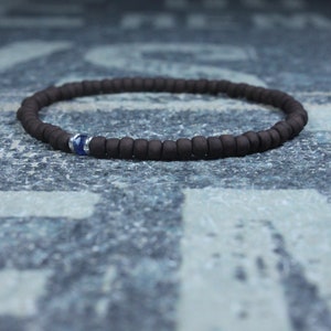 Puede incluir: Un brazalete de cuentas marrones con un solo acento de piedra preciosa azul.