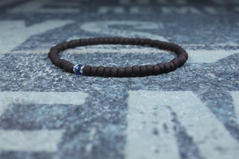 Puede incluir: Un brazalete de cuentas marrones con un solo acento de piedra preciosa azul.